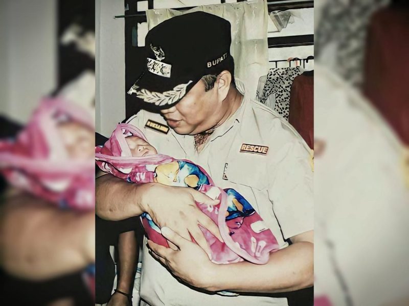 Dr. Ir. H. Ruksamin, S.T., M.Si., IPU., ASEAN Eng., terlihat dengan penuh kasih sayang menggendong salah satu bayi warga.